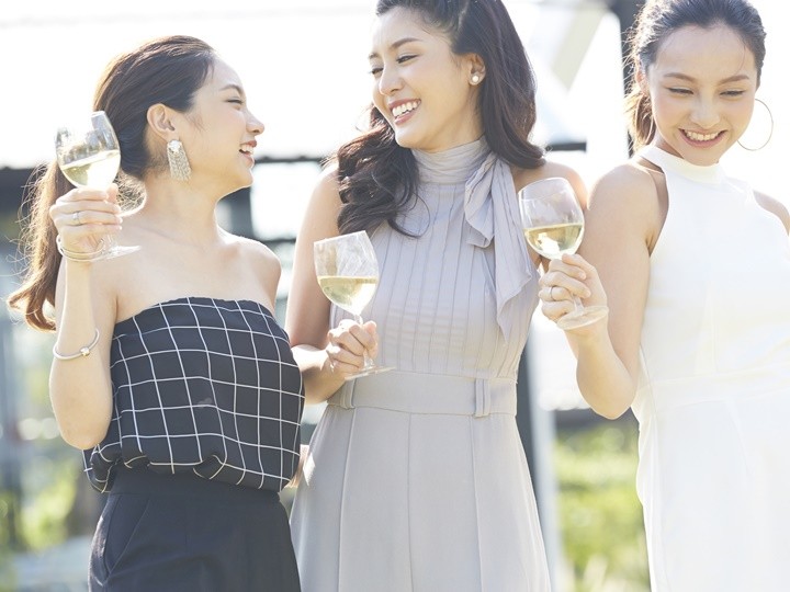 ガーデンパーティでワイングラスを手に笑い合う3人の20代女性